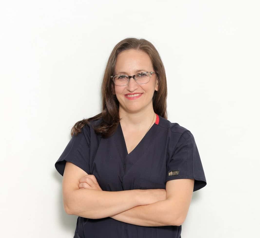 Female dentist with glasses smiling confidently in dental clinic.