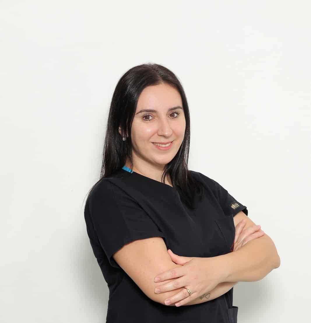 Smiling female dentist with crossed arms in black scrubs.